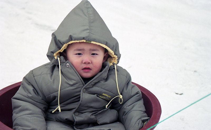 추운지 두꺼운 잠바를 입고 썰매를 타는 아이의 모습