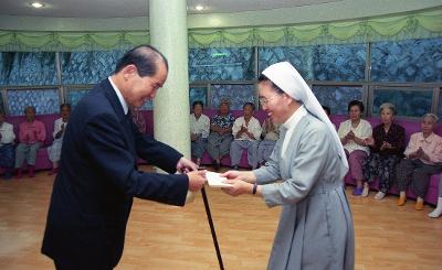 어르신들이 축하해주는 가운데 수녀님께 기념품을 받고 계신 시장님