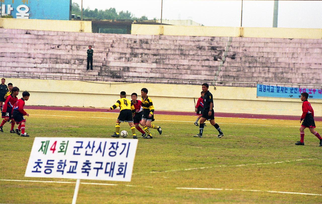 시장기 초등학교 축구대회를 알리는 팻말 뒤로 축구경기를 펼치고 있는 선수들