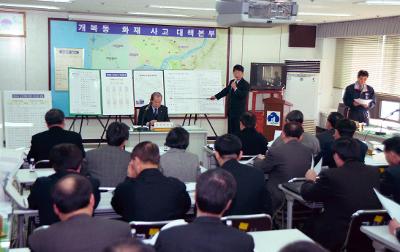 앞에서 자료를 가리키며 설명하고 계신 간부와 자리에 앉아 자료를 보고 계신 시장님과 간부들