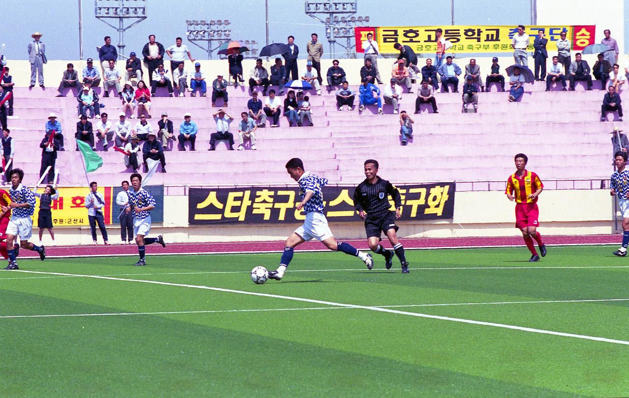 공을 몰고 달려가고 있는 선수와 뒤따라 뛰고 있는 주심