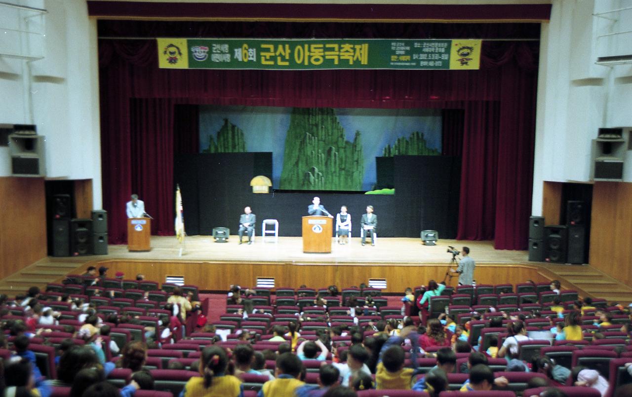 아동극 축제 무대 위에서 말씀을 하고 계신 시장님과 자리에 앉아 듣고 있는 아이들