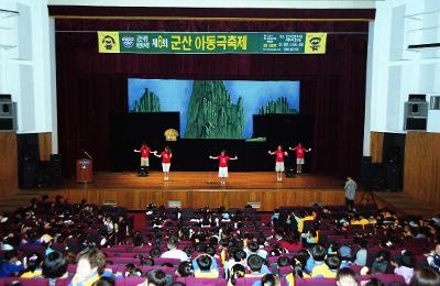 무대 위에서 아동극 축제가 열리고 있고 자리에 앉아 보고 있는 아이들