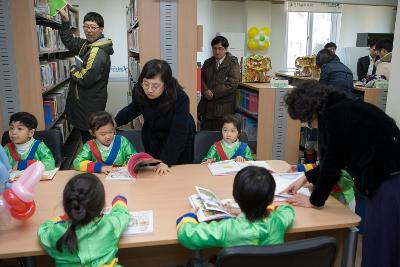 축하공연했던 아이들이 테이블에 둘러앉아 어른들의 도움을 받아 책을 보고 있는 모습1