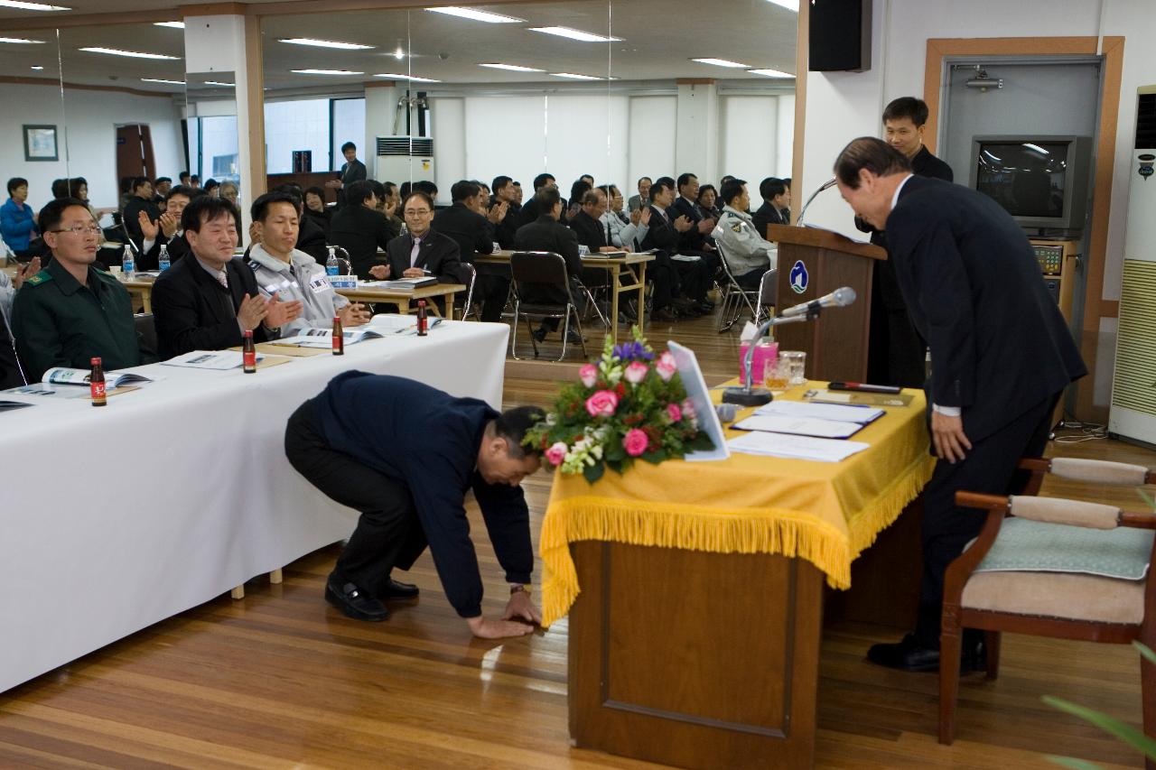 앞으로 나와 시장님께 절을 하고 있는 직원과 자리에서 일어나고 있는 시장님과 자리에 앉아서 보고 있는 직원들