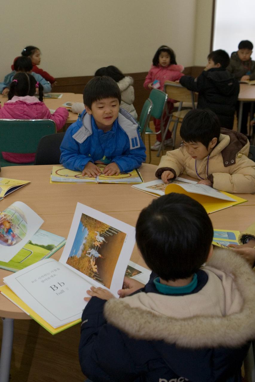 테이블에 둘러 앉아 책을 보며 이야기하고 있는 아이들1