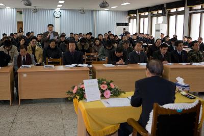 일어나 자료를 보며 말하고 계시는 직원과 듣고 있는 사람들과 시장님