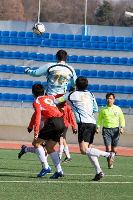 축구공을 향해 헤딩하는 선수들과 지켜보는 주심