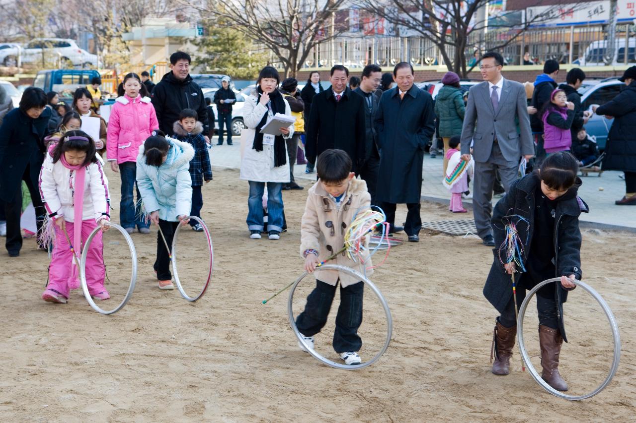 굴렁쇠를 굴리며 놀고 있는 아이들과 지켜보고 있는 어른들