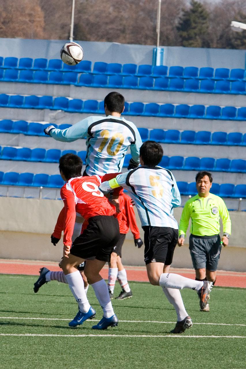 축구공을 향해 헤딩하는 선수들과 지켜보는 주심