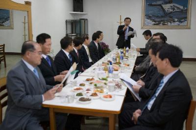 식사가 준비된 상 앞에 앉아 자료를 보며 말씀을 듣고 계신 시장님과 임원들