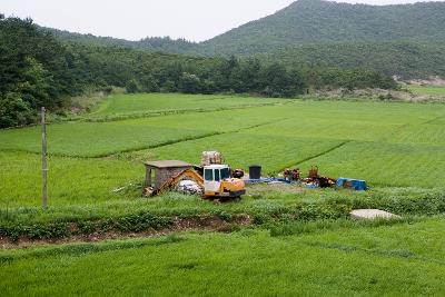 논들 가운데 포크레인과 경운기와 조그마한 건물의 모습1