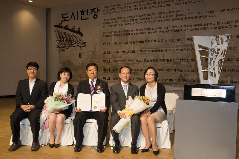 수여받은 상장과 꽃다발을 들고 의자에 앉아 사진을 찍고 있는 부시장님과 관련인사들