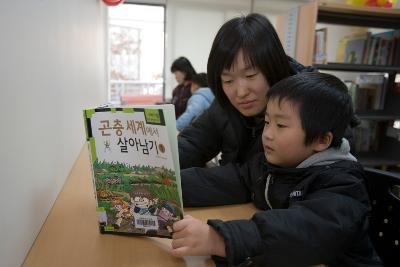 책상 앞에 앉아 아이와 함께 책을 보고 계신 어머님1