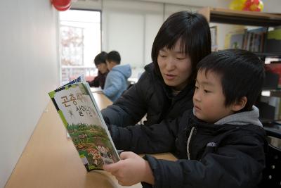 책상 앞에 앉아 아이와 함께 책을 보고 계신 어머님2