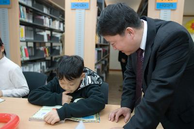 책상 앞에 앉아 책을 보고 있는 아이와 옆에서 말을 걸고 있는 관련인사